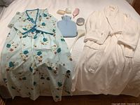 All items laid out on bed: both robes, hot water bottle, soap holder, back scrubber, Chanel compact