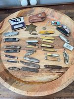 Overview of all knives, corkscrews, badge, sheath and lighter on wooden tray