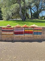 Four serape blankets folded over wall with four straw sombrero hats displayed on top