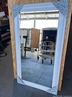 Full view of mirror with white frame leaning against wood panel