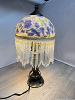 full view of lamp showing painted milk glass shade, beaded fringe, metal base and power cord
