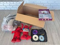 Group shot of all items: two Elmo dolls, CD binder, makeup kit, bag of neck pillows, boxed picnic table cover