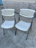 Front view of both white plastic folding chairs on black metal frames