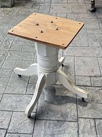 Full view of white wooden pedestal base with plywood top and casters