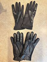 Both pairs of black leather gloves laid flat showing fronts and backs