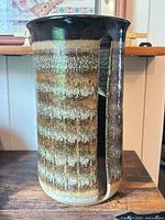 Front view of tall glazed ceramic cylinder showing slot opening and drip glaze