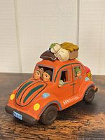 front left view of orange ceramic car figurine showing passengers and rooftop bundles