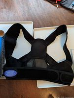 Black posture corrector brace front view showing straps and Velcro