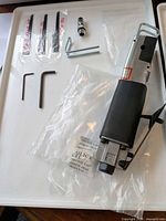 Unboxed saw showing zinc alloy body, rubber grip, blades, hex keys, coupler and manual on tray