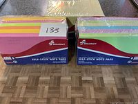 Front view of two boxed Skilcraft self-stick note pad packs and shrink-wrapped stack