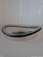 Oblique side view of freeform smoky gray glass bowl showing black rim and overall shape