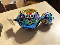 Side view of ornament showing blue body with floral glitter patterns, tag visible