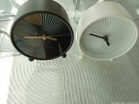 Front view of both black and white clocks on glass table