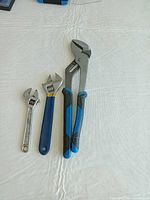 Three tools: two adjustable wrenches and tongue-and-groove pliers on white surface