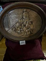 Front view of oval wooden relief carving depicting hockey scene