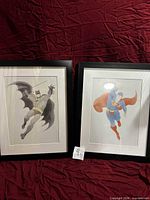 Both superhero prints in frames displayed side by side against red backdrop