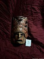 Front view of entire carved wooden mask beside size reference card