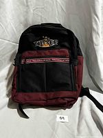 Front view of black and burgundy Tigger backpack showing embroidered logo and zip pocket