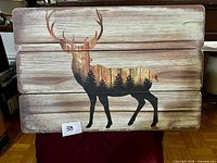 Front of wooden wall art showing deer silhouette with forest imagery on three plank panel