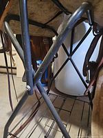 Overall view of black metal saddle stand under saddle showing X-frame legs and hardware