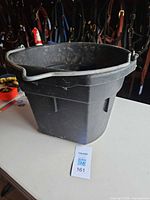 Full exterior view of black plastic bucket on table with handle upright