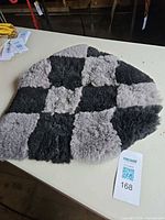 Full view of checkerboard sheepskin seat pad on table with lot tag