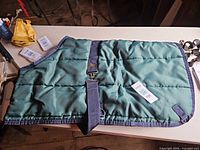 Full view of teal and navy horse blanket laid flat showing quilted construction and surcingle strap
