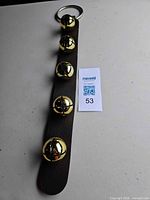 Front view showing five gold bells on brown strap with key ring