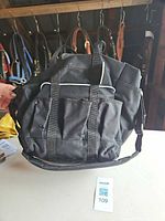 Front view of black nylon tote bag showing pockets, handles, shoulder strap