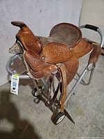 Full view of tooled leather Western saddle on stand with attached straps and girth