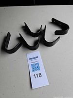 Five black metal hooks laid out face up next to lot tag