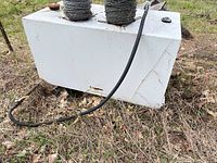 White steel fuel transfer tank with attached black hose lying on ground