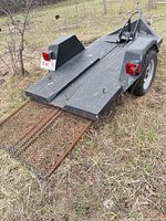 Full view of trailer left rear showing expanded metal ramp, tail lights, wheel