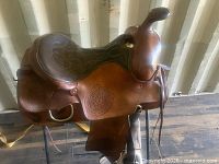 Left side view of saddle showing tooling, horn, fender, stirrup, and maker’s stamp