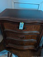 Front view of one dresser showing three drawers, serpentine front, brass-tone pulls