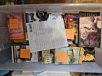 Plastic tote containing multiple stacks of paperback books with visible titles by Robin Lee Hatcher, Kathy Herman, Lynette Eason and Love Inspired Suspense series.