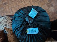 Sleeping bag compressed in black stuff sack with camo fabric visible at opening and auction tag attached