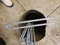 Top view of bucket containing six galvanized steel ground anchors with eyelet ends