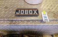 Close view of Jobox badge on diamond plate aluminum surface of truck tool box, shows latch area and wear