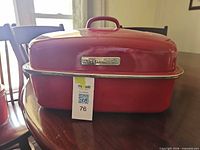 KitchenAid red enameled roasting pan with domed lid on dining table, lot tag visible