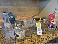 Group shot of Pepsi bottle, Mason jars, plastic tub with wooden lid, and maple syrup jug on countertop