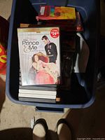 Top view of blue storage tote containing multiple DVD cases; visible title The Prince & Me on top