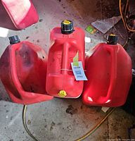 Front view of three red fuel cans showing spout caps and overall wear