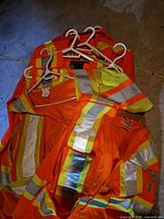 Pile of multiple hi-vis jackets and vests on hangers showing reflective tape and colours