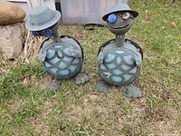 Two metal turtle figures showing hats, lens bodies and surface wear