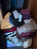 Stack of mixed towels and folded sheets in closet space with lot tag visible