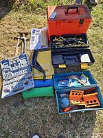 Full lot overview on grass showing Husqvarna case, toolboxes, accessory kits, hammers, ropes and clamps