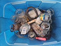Blue tote containing glass jars of hardware, wire brushes, belts and rope