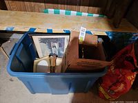 Overview of blue storage tote and contents: framed print, picture frames, brass item, cardboard box