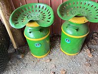 Two green/yellow John Deere tractor seat stools on milk can bases